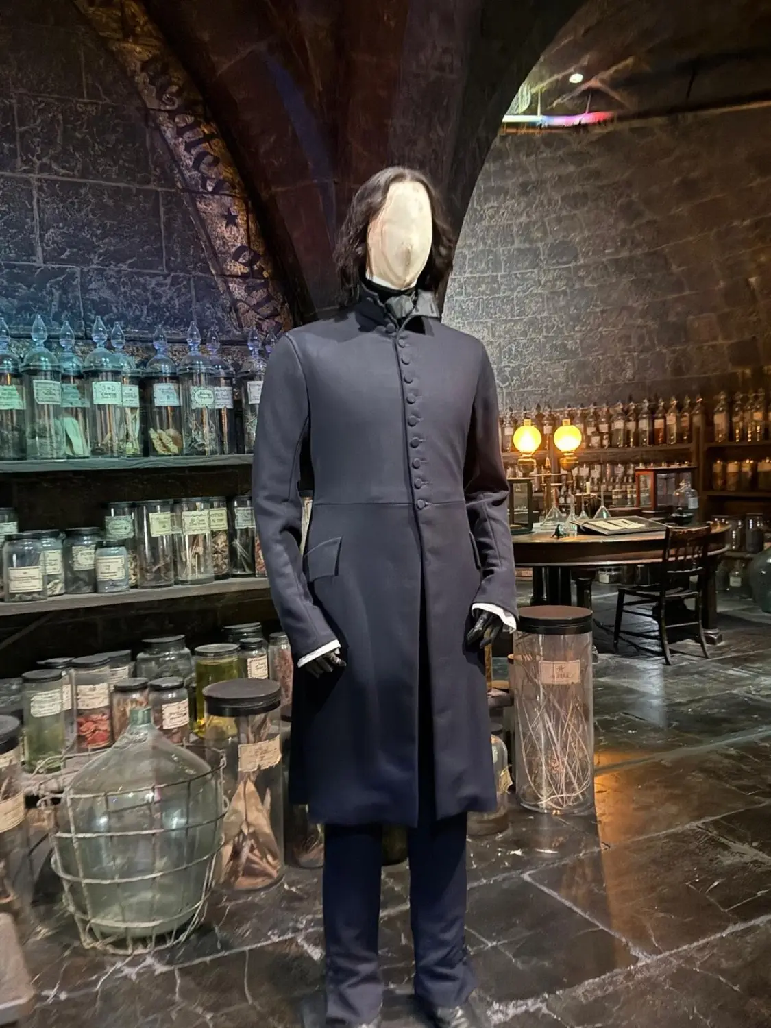 A headless mannequin dressed in Professor Snape’s long black robes, displayed inside a detailed potions classroom set filled with shelves of labelled jars, cauldrons, and magical ingredients.