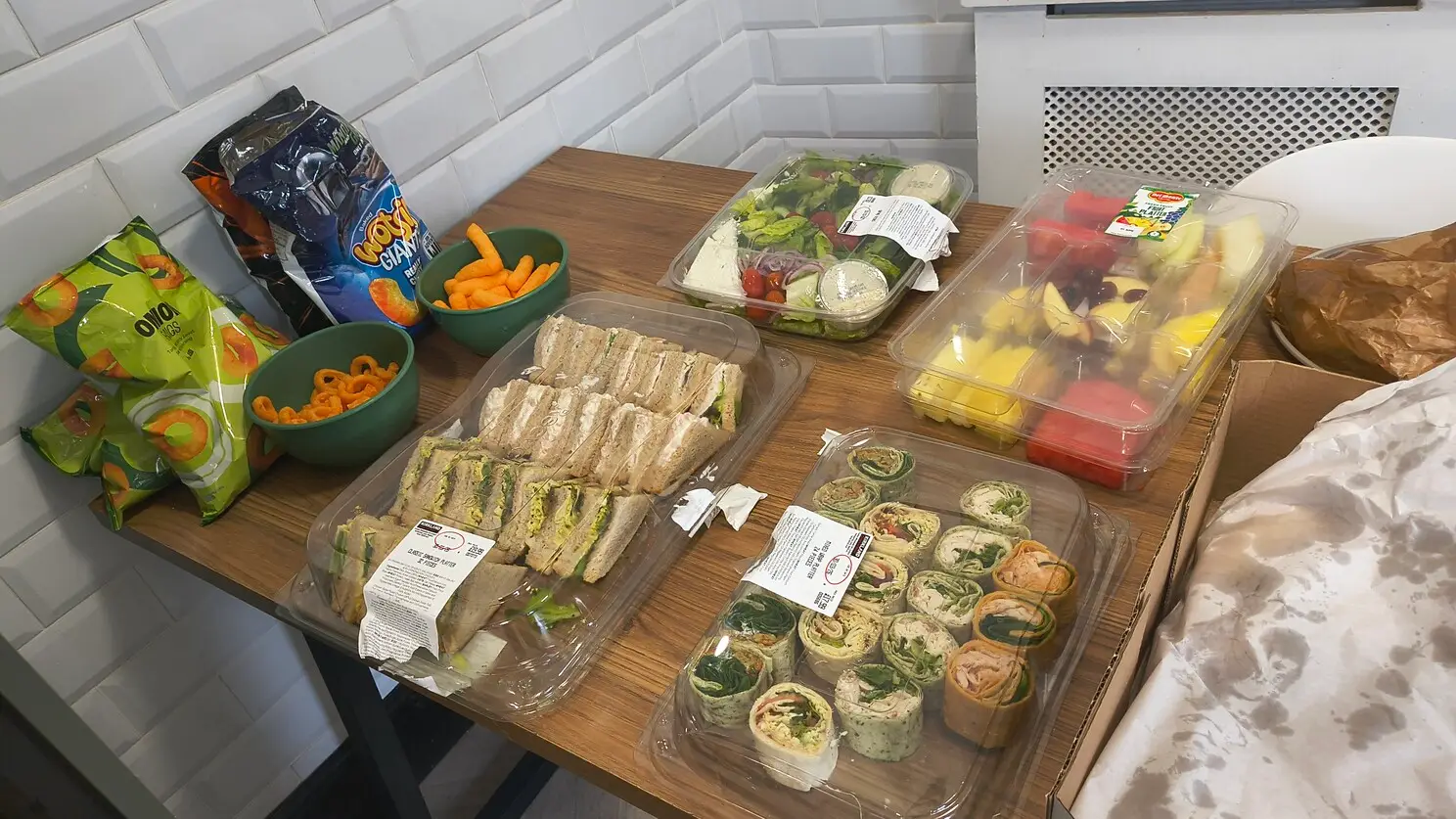 Sandwiches, wraps, various fruits, salad and crisps.