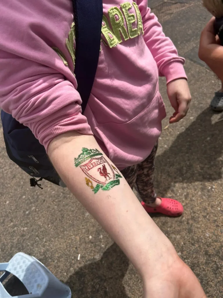 YP applies her favourite football teams logo, Liverpool F.C. glitter temporary tattoo on her arm.