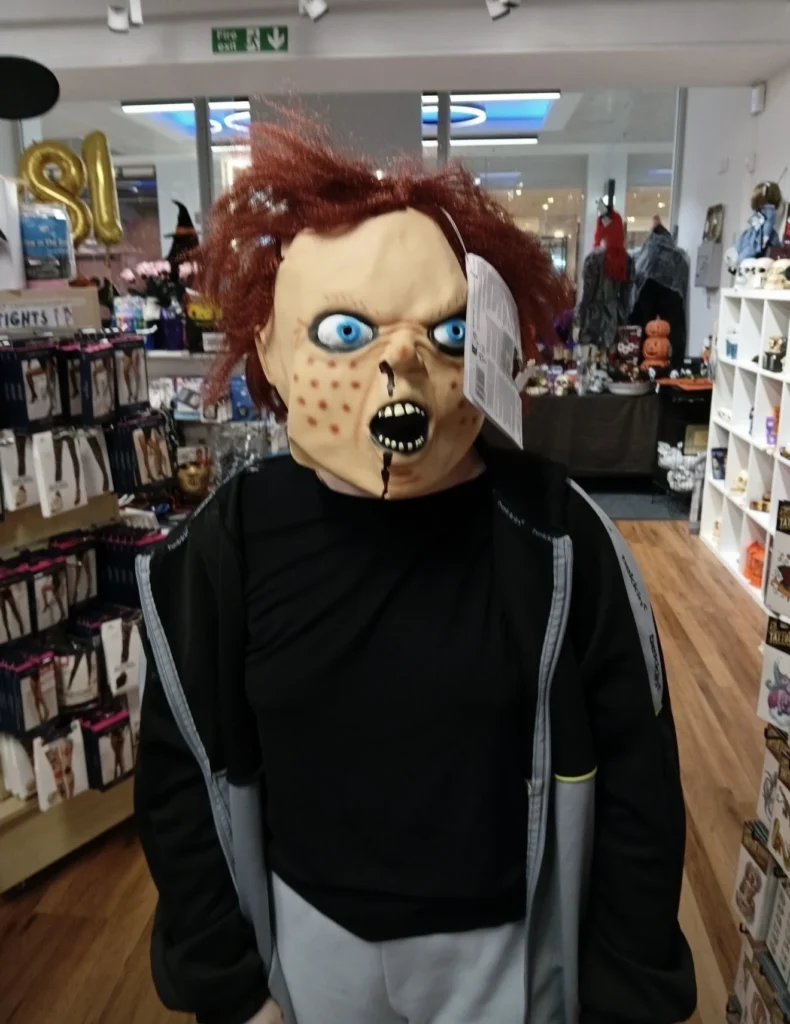 Young person trying on a Halloween character mask while exploring seasonal displays and decorations at B&M.