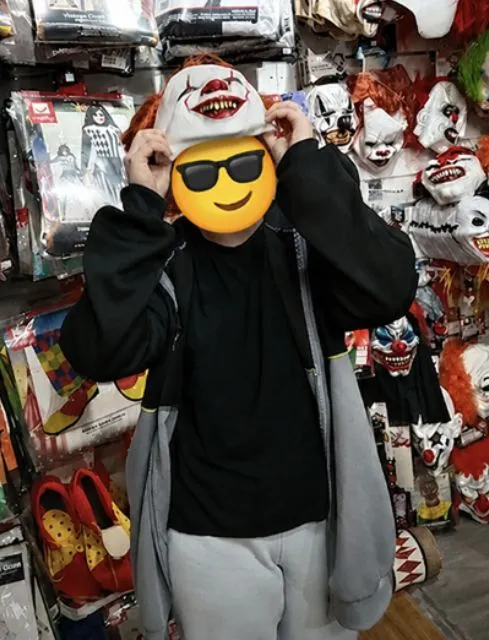 Young person trying on a Halloween clown mask while browsing seasonal costumes and decorations at B&M.