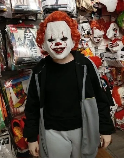 Young person trying on a Pennywise-style Halloween mask while exploring seasonal costume displays in B&M.